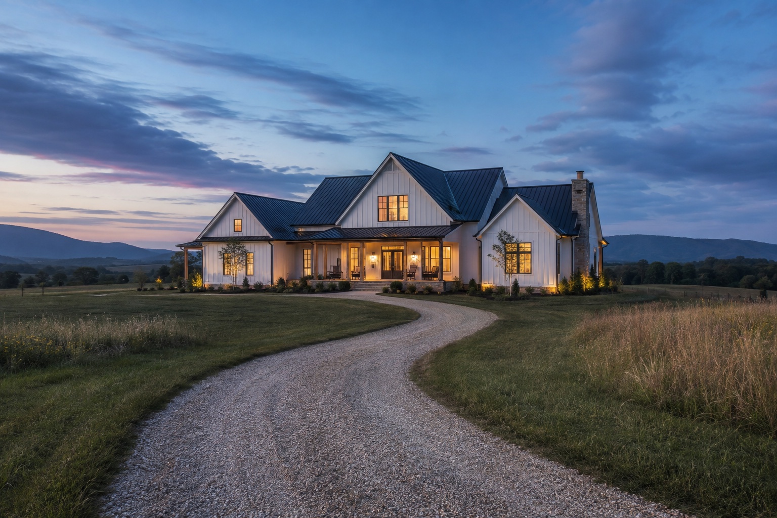 Country farmhouse at twilight with warm porch lights and a long gravel drive